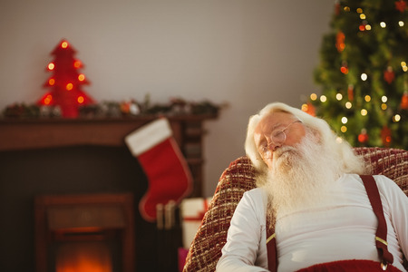Father christmas resting on the armchair at home in the living roomの写真素材