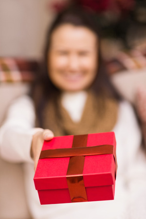 Brunette woman offering christmas gift at home in the living roomの写真素材