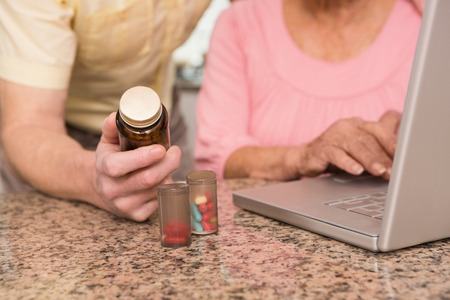 Senior couple looking up medication online at home in the kitchenの写真素材
