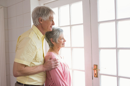 Senior couple looking out their window at home in the kitchenの写真素材