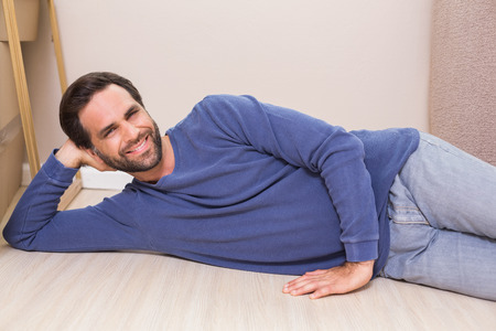 Happy man lying on floor with moving boxes in his new homeの写真素材