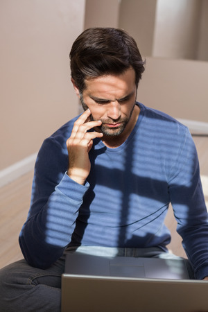 Depressed man sitting on floor using laptop in an empty roomの写真素材