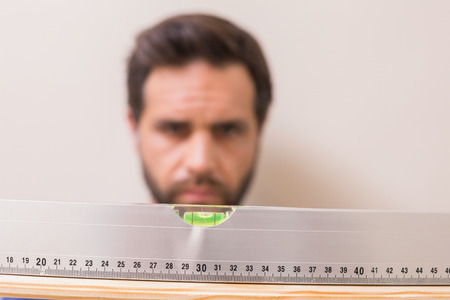 Casual man using spirit level at home in the living roomの写真素材