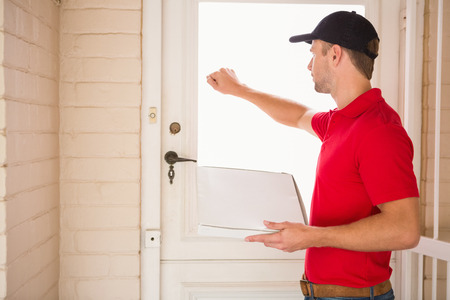 Delivery man holding pizza while knocking on the door to a houseの写真素材