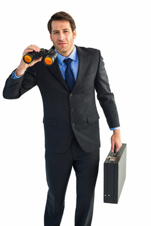 Serious businessman holding binoculars and a briefcase on white backgroundの写真素材