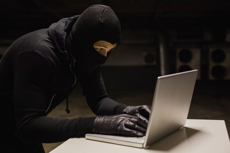 Robber at desk hacking a laptop on black backgroundの写真素材