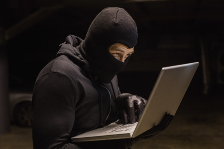 Focused burglar standing holding laptop on black background