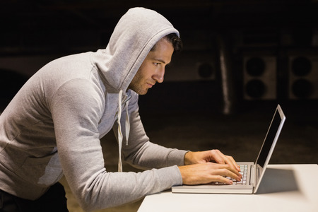 Man in hood jacket hacking a laptop on black backgroundの写真素材