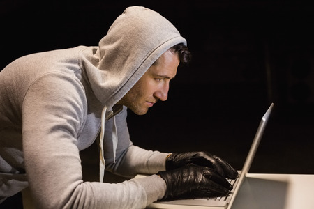 Man in hood jacket hacking a laptop on black backgroundの写真素材