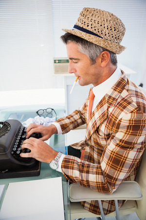 Vintage man in straw hat typing on typewriter in his officeの写真素材