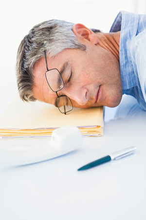 Man with glasses sleeping on his files on desk in his officeの写真素材