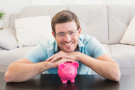 Smiling man with a piggy bank at home in the living roomの写真素材