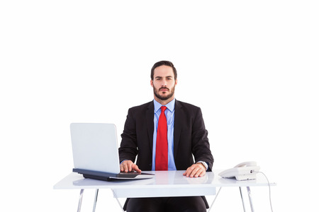 Unsmiling businessman sitting at desk  on white backgroundの写真素材