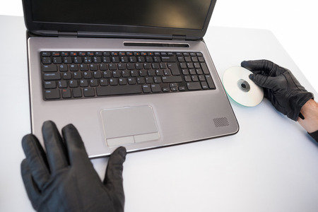 Burglar hacking and putting a cd-rom in laptop on white background