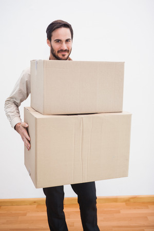 Smiling man holding a cardboard moving box in the living roomの写真素材