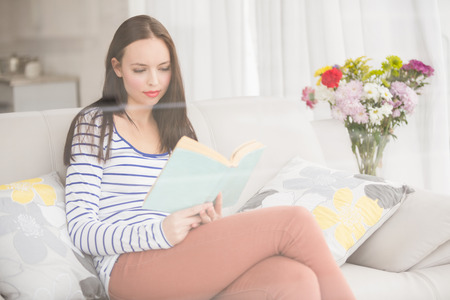 Pretty brunette reading book on couch at home in the living roomの写真素材