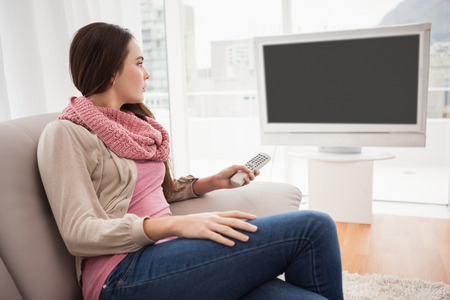 Pretty brunette watching tv on couch at home in the living roomの写真素材