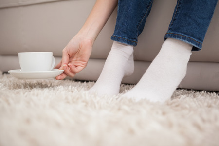 Woman picking up cup and saucer at home in the living roomの写真素材