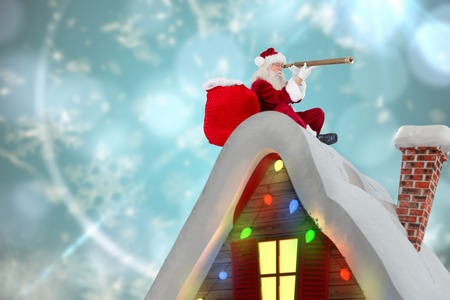 Santa sitting on roof of cottage against blurred christmas backgroundの写真素材