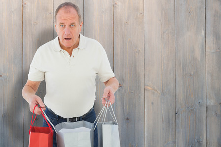 Shocked man holding shopping bags against pale grey wooden planksの写真素材