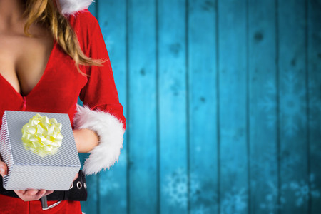 Sexy santa girl holding gift against blurred snowflakes on planksの写真素材