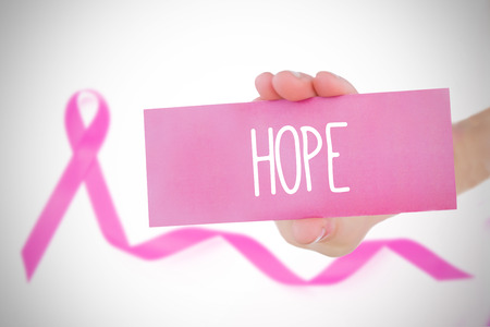 Young woman holding pink card against pink awareness ribbon with trailの写真素材