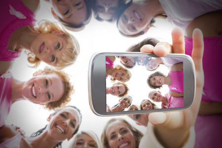 Composite image of hand holding smartphone showing photograph of breast cancer activists