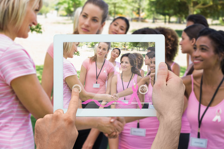 Composite image of hand holding device showing photograph of breast cancer activistsの写真素材