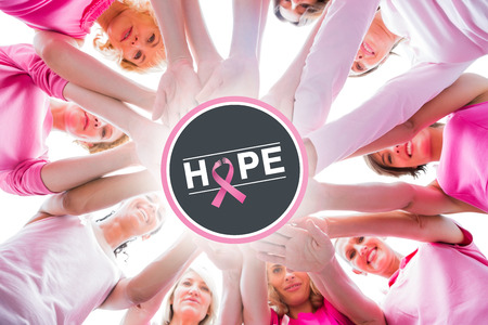 Diverse women smiling in circle wearing pink for breast cancer against breast cancer awareness message on posterの写真素材