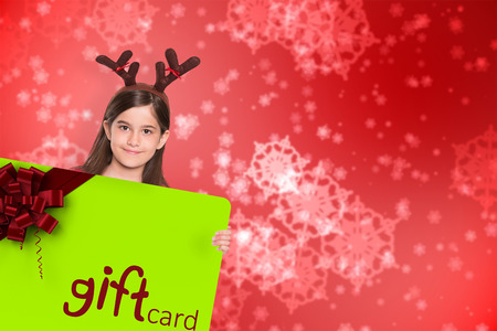 Festive little girl showing card against digitally generated delicate snowflake designの写真素材