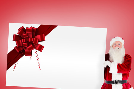 Santa claus showing card with red christmas ribbonの写真素材