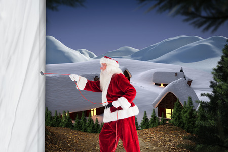 Santa pulls something with a rope against cute village in the snowの写真素材