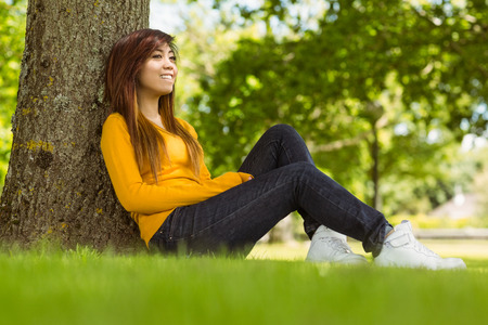Side view of beautiful young woman sitting against tree in the parkの写真素材