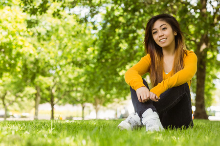 Portrait of beautiful relaxed young woman sitting on grass at the parkの写真素材