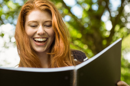 Cheerful female college student reading book in the parkの写真素材