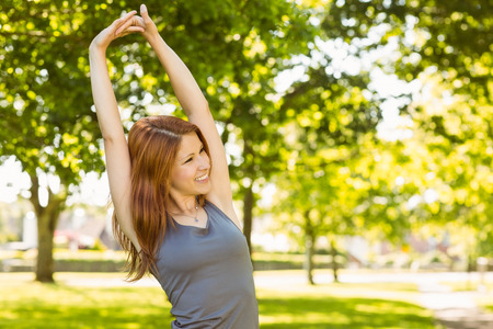 Pretty redhead stretching in the park on a sunny dayの写真素材