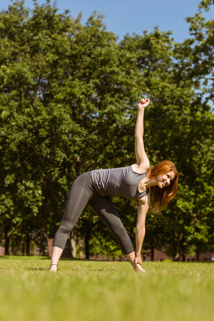Pretty athletic redhead stretching in park in a sunny dayの写真素材