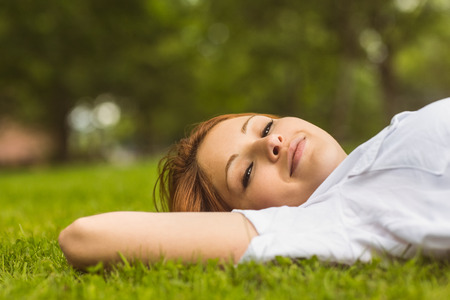 Pretty redhead smiling and lying on grass in parkの写真素材