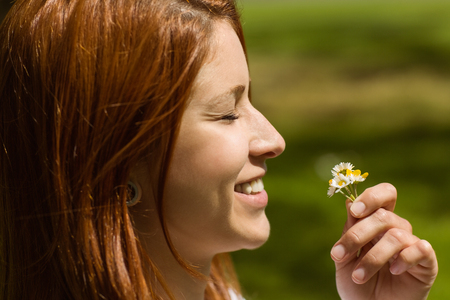Portrait of a pretty redhead holding flowers on a sunny dayの写真素材