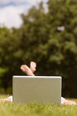 Pretty redhead lying with her laptop on grass in parkの写真素材