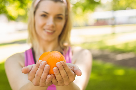 Fit blonde holding an orange on a sunny dayの写真素材