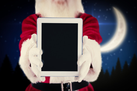 Santa presents a tablet PC against crescent moon over forest at nightの写真素材