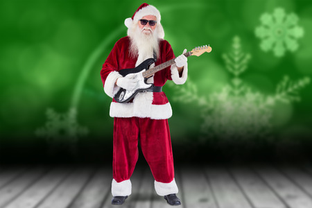 Santa Claus plays guitar with sunglasses against shimmering light design over boardsの写真素材