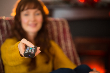 Smiling redhead holding remote control at christmas at home in the living roomの写真素材