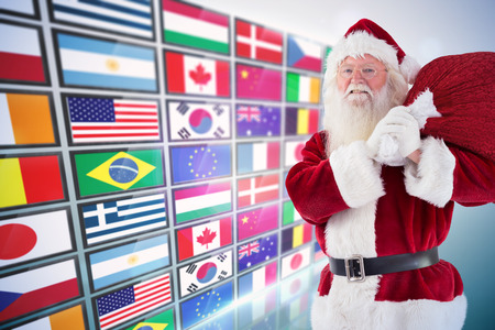 Santa carries his red bag and smiles against screen collage showing international flagsの写真素材