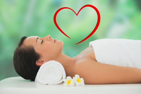 Beautiful brunette relaxing on massage table against heartの写真素材