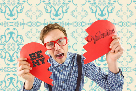 Geeky hipster holding a broken heart  against elegant patterned wallpaper in blue and creamの写真素材