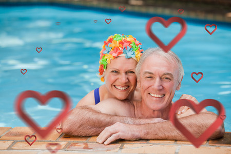 Happy mature couple in the swimming pool  against heartsの写真素材