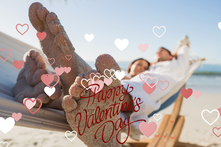 Close up of sandy feet of couple in a hammock against happy valentines dayの写真素材