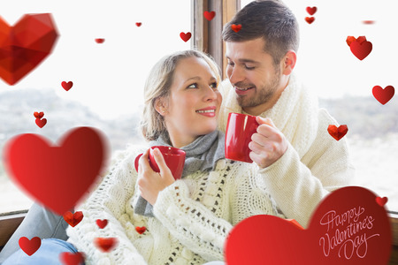 Loving couple in winter wear drinking coffee against window against cute valentines messageの写真素材
